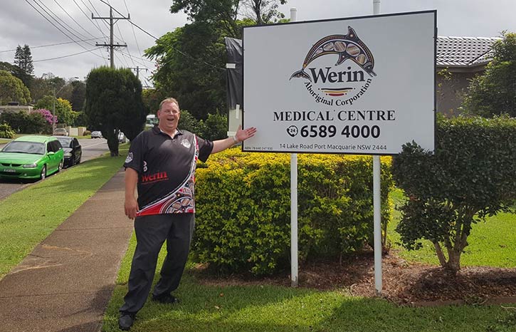 Man standing proudlly in front of a sign for Werin Aboriginal Corporation
