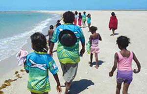 Adults and children walking along a white sandy beach away from the camera
