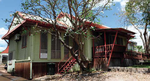House with green walls, red roof and railings and trees out the front