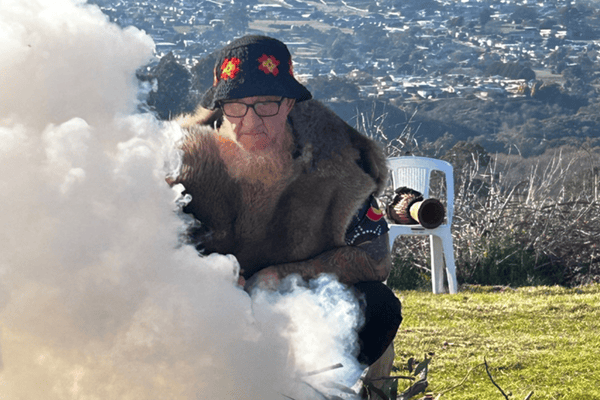 A man leans over a small outdoor fire