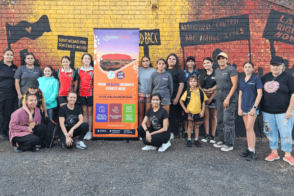 A group of people pose in front of a wall with land rights artwork painted on it