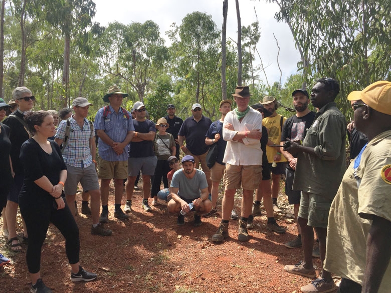 A group of people dressed for an outdoor walk stand in a group listening to a guide