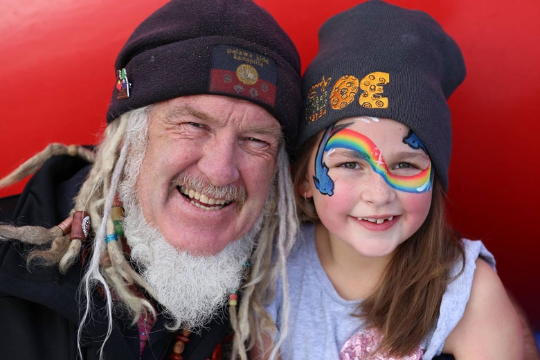An older man poses with a young girl whose face is painted with a rainbow
