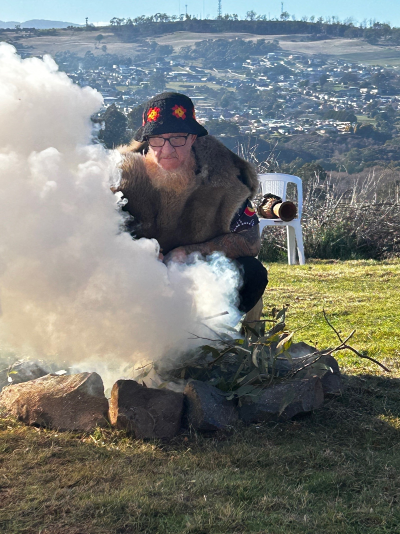 A man leans over a small outdoor fire