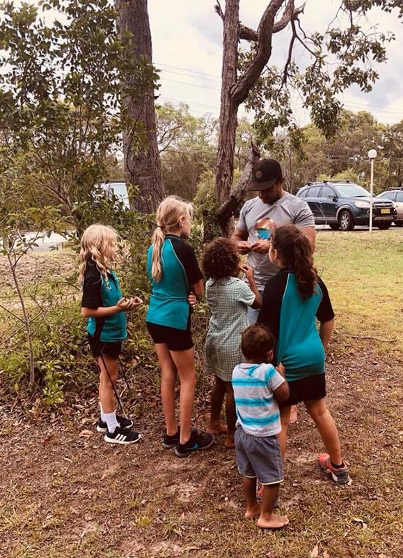 A man with a small group of children under a tree