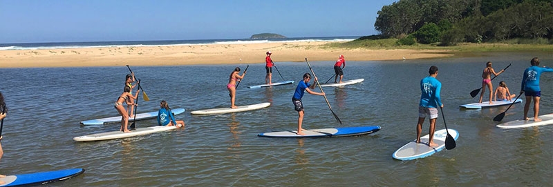 A group of people stand on boards in calm water