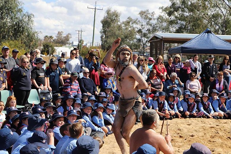 An Aboriginal man dances watched by a crowd of people