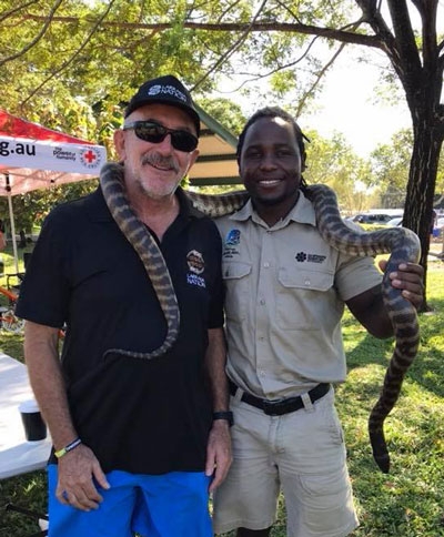 Two men stand with a snake draped around their shoulders