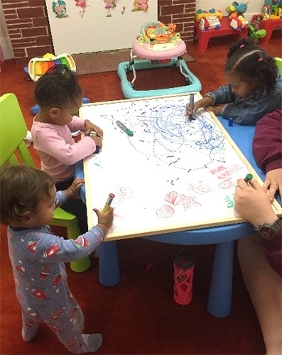 Small children draw on a large piece of paper on a low table