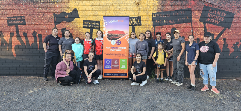 A group of people pose in front of a wall with land rights artwork painted on it