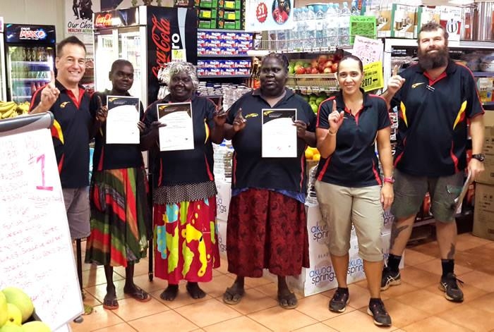 A group of people pose in a store. Three of them are holding certificates