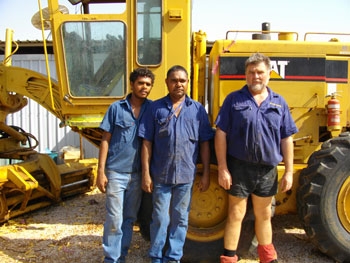 Three men stand in front of a large piece of machinery
