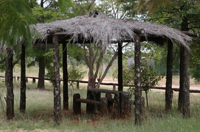 An open-sided shelter with a grass roof and table and chairs made from logs