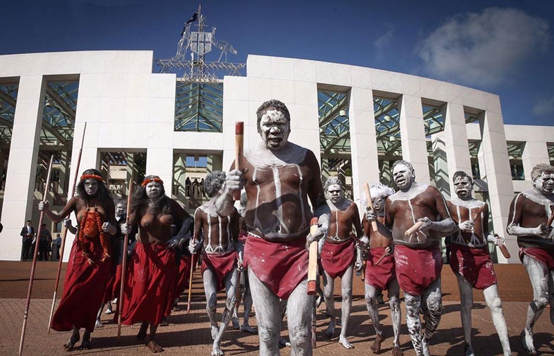 A group of Aboriginal people in traditional cultural dress and body paint in front of Parliament House in Canberra