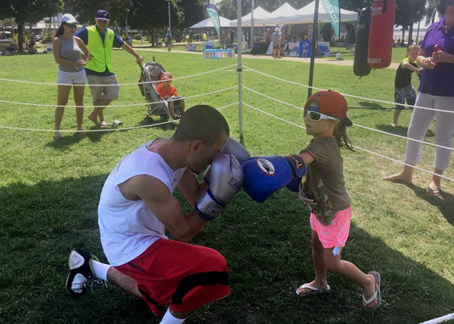 A man wearing boxing gloves pretends to fight with a young child in a grassy area