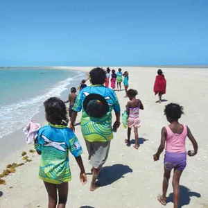 An adult and a number of children walking on a beach