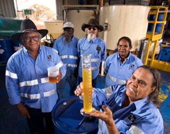 A group of people in matching blue shirts look at a beaker of yellow liquid another person is holding up