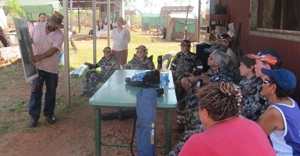 A man stands in front of a group of people gesturing at a large document he's holding up