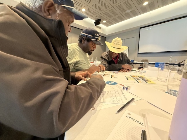 Three men with paperwork sit at a table