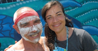 Two people smile at the camera. One is wearing traditional face paint