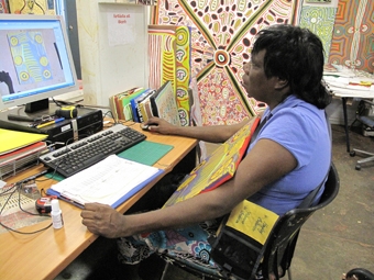 A woman working at a computer. Behind her hangs a large painting