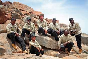 A group of men in khaki shirts and dark pants pose together on a rocky outcrop