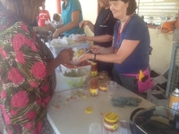 A table with taco ingredients. One woman hands food to a woman on the other side of the table