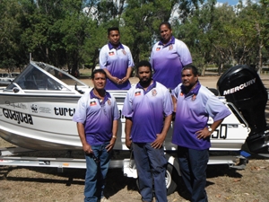 A group of people all wearing the same purple shirt stand with a boat on a trailer