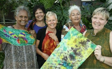 A group of 5 women smile at the camera. Two of them are holding up artworks
