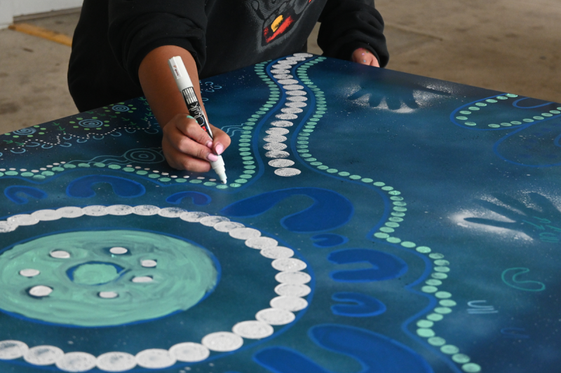 A person's hand with a white marker drawing on a blue and white artwork