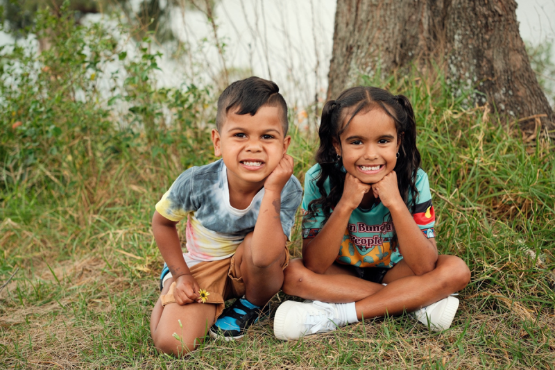 Two smiling children sitting on grass