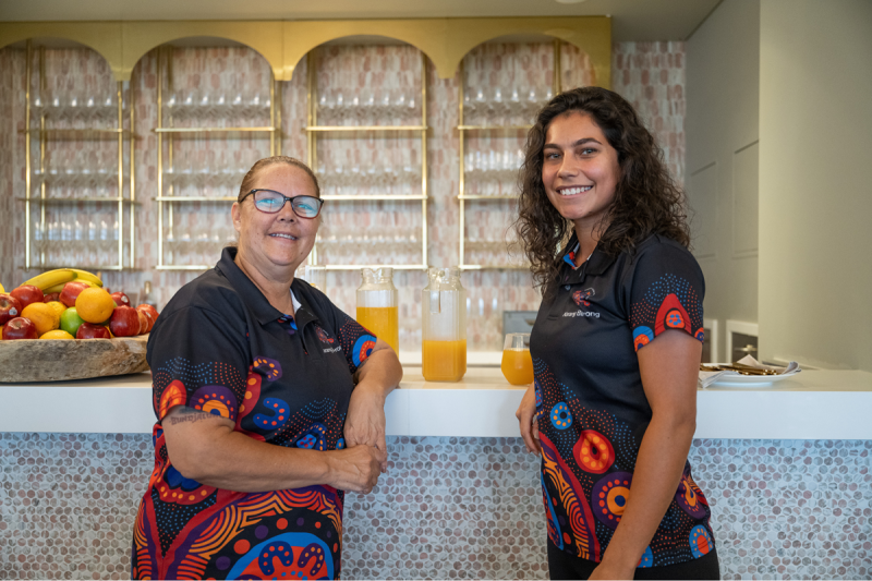 Two women in matching shirts smile at the camera