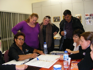 A group of people sit and stand around a table with paperwork on it