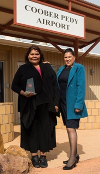 Two women standing under a sign saying Coober Pedy Airport. One of the women is holding an award.