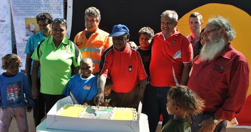A group of people standing around a table with a large cake on it