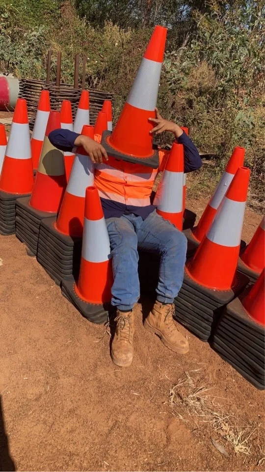 A person wearing hi vis and work boots with a traffic cone over their head
