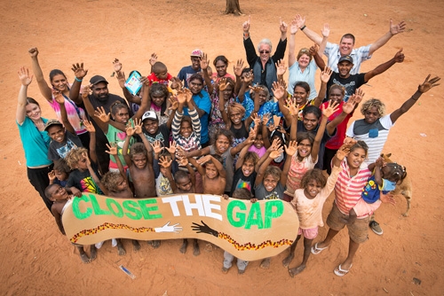 An overhead photo of a group of people holding a hand-painted banner that reads 'close the gap'
