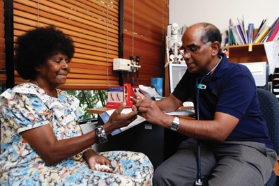 A woman sits while a doctor examines her hand