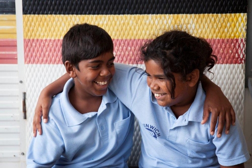 Two children in school uniforms with their arms around each other