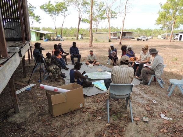 A group of people sit in a rough circle in an outdoor area