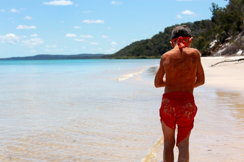 A young person walks on a beach with their back to the camera