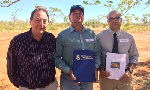Three men stand in an outdoor location. Two of them are holding documents