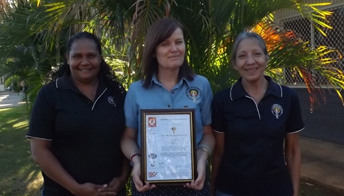 Three women face the camera. The middle woman is holding a certificate