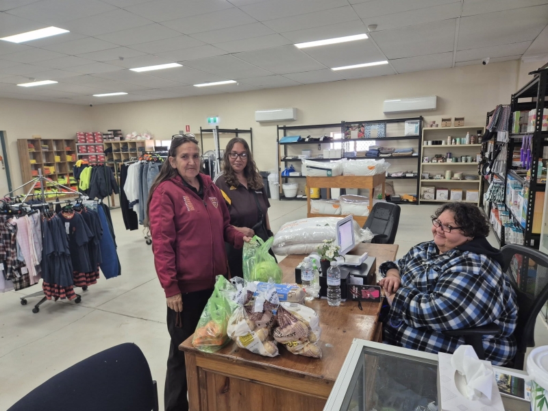 A woman sits behind the counter of a store. Two women stand at the counter.
