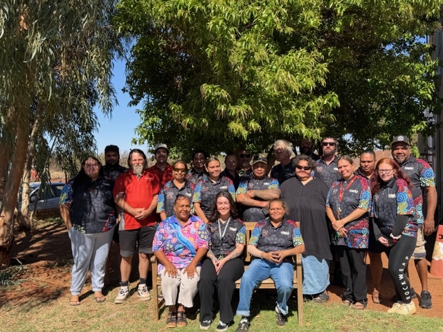 A large group of people pose for the camera with trees behind them